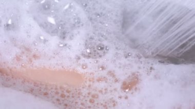 Kadın köpüklü bir duş alıyor. O vücudu duş su dökülen. Köpük yakın çekim.