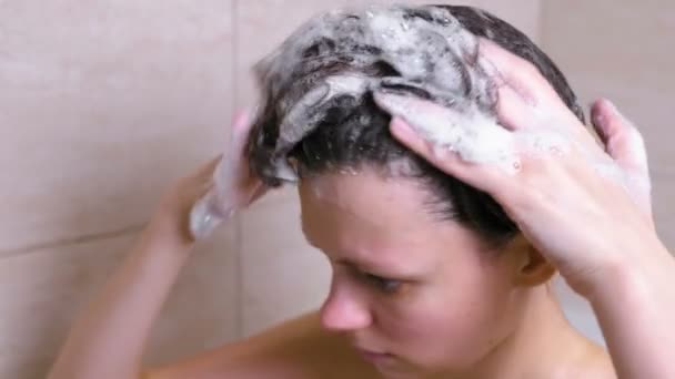 La mujer se lava la cabeza y los pelos con champú en el baño . — Vídeos de Stock