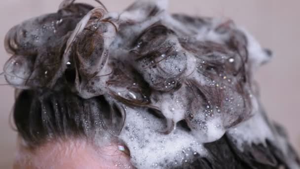 La mujer se lava la cabeza y los pelos con champú en el baño. Masaje de primer plano con las manos . — Vídeos de Stock