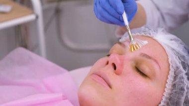 Güzellik uzmanı fırça ile kadının yüzünde maske koyar. Yüz nemlendirici. Yüz yakın çekim.