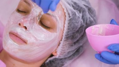 Güzellik uzmanı fırça ile kadının yüzünde maske koyar. Yüz nemlendirici. Yüz yakın çekim.