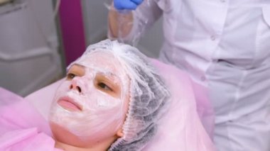 Güzellik uzmanı nemlendirici maske üstüne plastik bir film kadının yüzüne koyar..