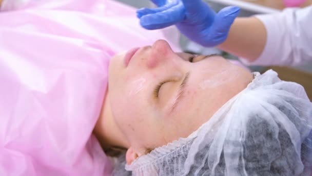 Schoonheidsspecialist zet de moisturizer crème op dames gezicht. Close-up gezicht. — Stockvideo