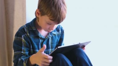 Seroisly çocuk pencere içinde oturan tablet oyun oynuyor.