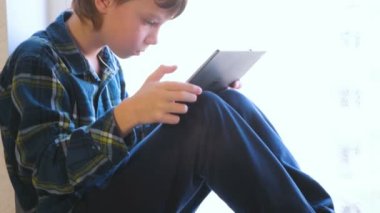 Seroisly çocuk pencere içinde oturan tablet bir video izlerken.