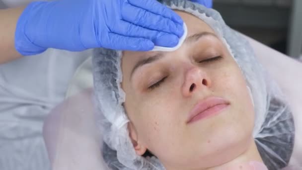 Cosmetologist limpa o rosto de uma jovem mulher com almofadas de algodão. As mãos do esteticista em luvas e uma cara fecham-se. Tratamentos de beleza para o rosto . — Vídeo de Stock