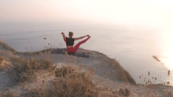 Вид женщины, занимающейся йогой Upavista Konasana, Широкая сидячая согнутая поза на горе с видом на море на закате . — стоковое видео