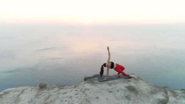 Красива жінка робить йога Vasisthasana, стороні дощата позувати на вершині гори з видом на море на захід сонця повітряних кадри. — стокове відео