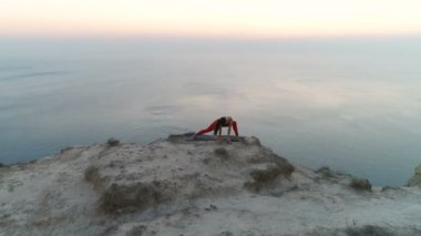 Güzel sportif kadın yoga stretcing gün batımında deniz manzaralı dağ tepesinde yapıyor. Havadan görüntüleri.