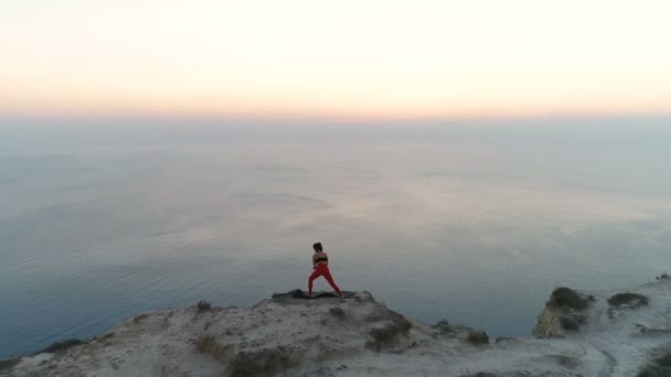 Hermosa mujer se extiende en la cima de la montaña con vista al mar al atardecer. Imágenes aéreas. Vista trasera . — Vídeos de Stock