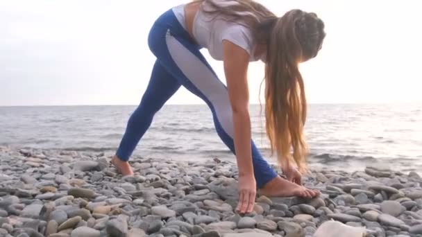 Schöne Frau macht Yoga auf Steinbach mit Meerblick bei Sonnenuntergang. — Stockvideo