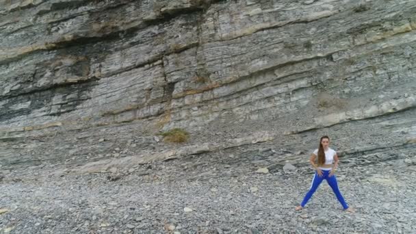 女性は岩の背景に呼吸中、bodyflex プリエ スクワットをやっています。空中の美しい映像表示. — ストック動画