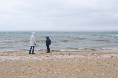 Anne ve oğlu kış, arka görünümünde deniz kum plajda yürüyor. Kum ve kar fırtına güzel manzarasını plaj.