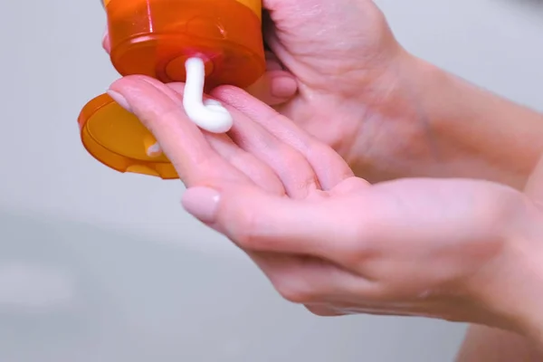 Женщина кладет шампунь из оранжевой бутылки в руку, чтобы вымыть голову. Руки крупным планом . — стоковое фото