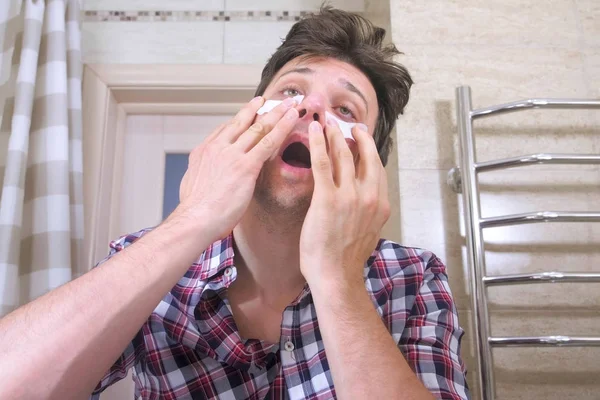 Loco hombre despertado con una resaca elimina los parches de los ojos en el baño . —  Fotos de Stock