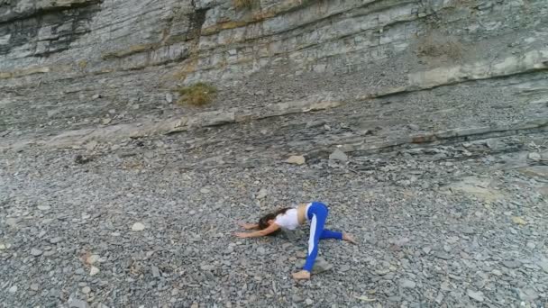 Žena dělá jógu a stretcing bodyflex cvičení na pozadí rock a moře. Letecké záběry krásné boční pohled. — Stock video