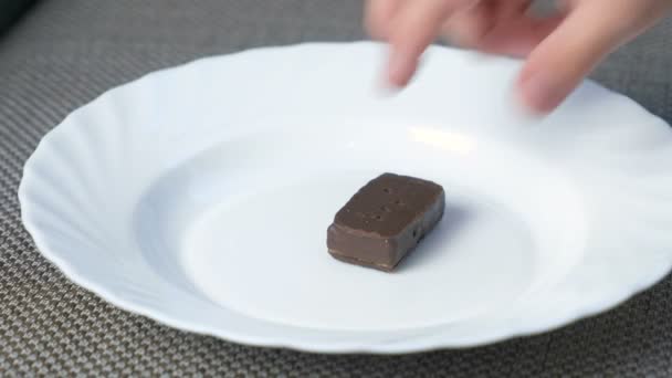 Childs hand zetten een chocolade snoepjes op een witte plaat. — Stockvideo