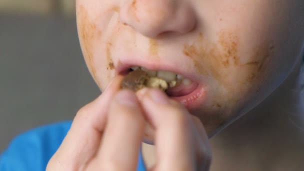 Grimy happy teen boy is eating chocolate candy sitting on the sofa. Concept of unhealthy eating. Mouth Close-up. — Stock Video