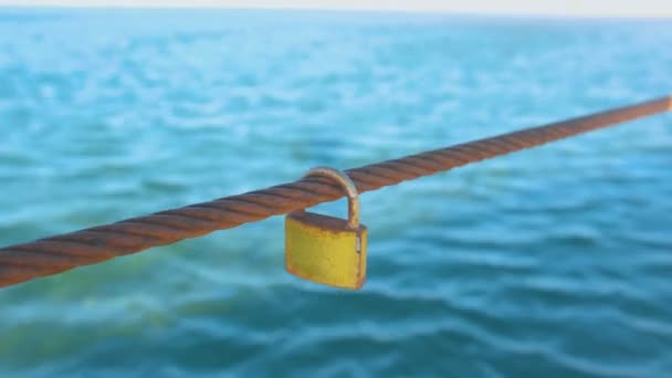 Rusty Padlock opknoping op een ijzerdraad op de achtergrond van de zee water. — Stockvideo
