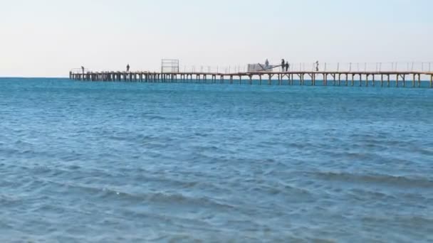 La gente está caminando sobre un viejo muelle de madera en el mar. Vista lateral . — Vídeos de Stock