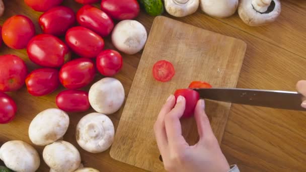 Womans hands is cutting tomatoes on the wooden bord on kitchen table. Top view. — Stock Video