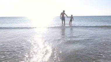 Baba ve oğlu tarafından deniz suyu günbatımı üzerinde yürüyor. Denizde yüzme.