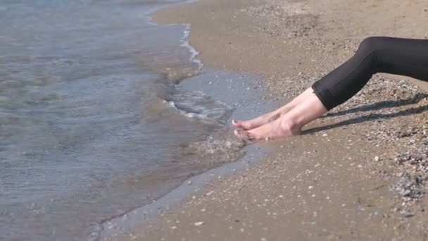Womens voeten in leggins tegen de zee in zandstrand. Zijaanzicht. — Stockvideo