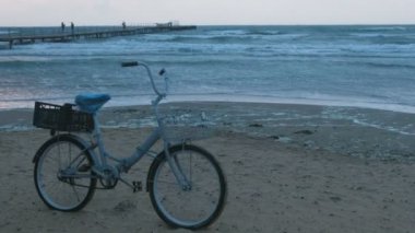 Fırtına deniz ve köpük ile gün batımında sahilde eski bisiklet arka plan ve İskelesi ile insanlar yürüyen dalgalar.
