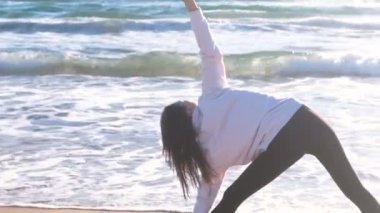Kadın yoga kum plaj dalgalar ile yapıyor. Genişletilmiş üçgen poz içinde ayakta, arkadan görünüm.