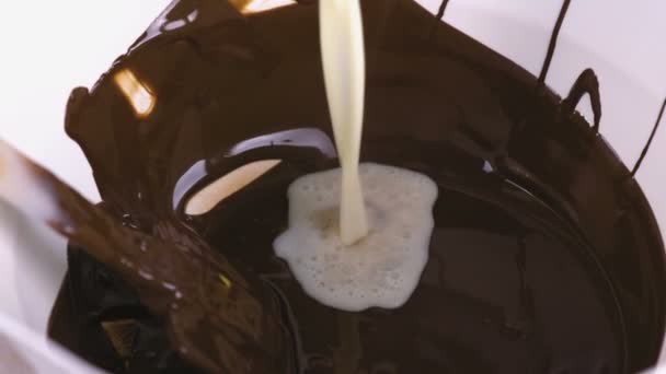Pour cream and mix liquid dark chocolate in a white bowl with spatula. Close-up view. — Stock Video