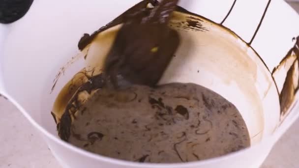 Mezclar el chocolate negro líquido con crema en un tazón blanco con espátula. Vista de primer plano . — Vídeos de Stock