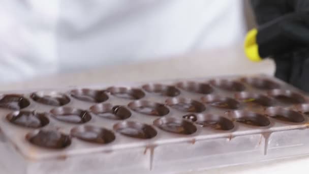 Bäckerhände entfernen überschüssige Schokolade mit einem Spachtel aus der Form. — Stockvideo