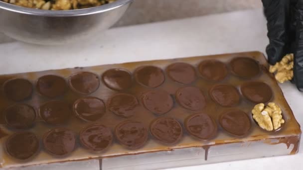 Mains boulangers mettre les moitiés de noix sur les bonbons au chocolat dans les formes . — Video