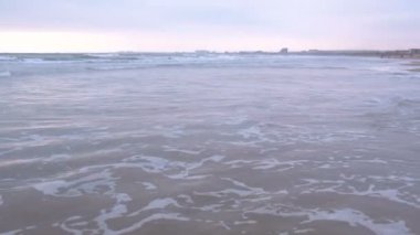 Büyük fırtınalı dalgalar deniz. Kumlu plaj ve kıyı kenti gün batımında arka plan üzerinde güzel deniz manzarası.