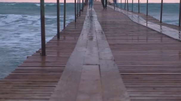 La familia está huyendo de las olas en el muelle del mar en tormenta. Olas salpicaduras a través del muelle de madera en el mar. Hermoso paisaje marino al atardecer. Primer plano de las piernas . — Vídeos de Stock