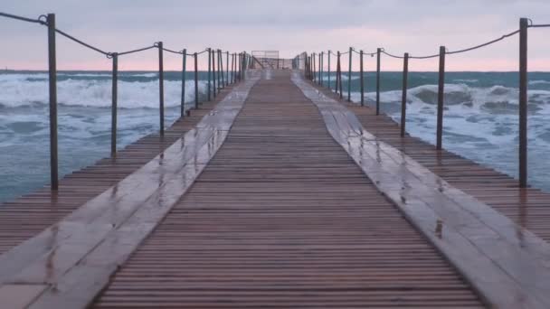 Vlny šplouchat přes dřevěné molo v moři. Krásná krajina při západu slunce. — Stock video