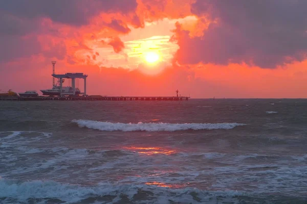 Indah pemandangan laut dengan matahari terbenam merah, pelabuhan laut dengan kapal dan gelombang badai di malam hari . — Stok Foto