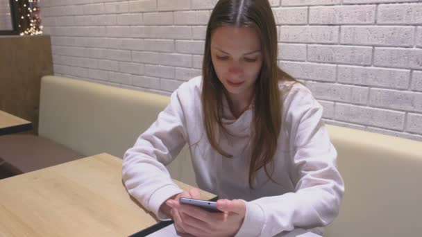 Žena je psaní zprávy na mobilním telefonu sedí a čeká, někdo v kavárně. — Stock video