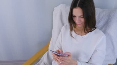 Mutlu genç esmer kadın bir sandalyede oturan bir cep telefonunda bir mesaj türleri.