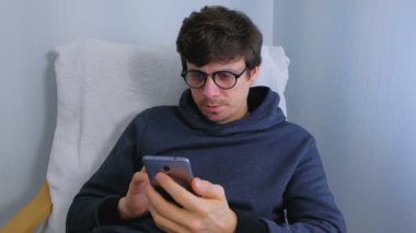 Gözlüklü adam koltuğa oturan Smartphone cep telefonu ile sosyal medya tarama.