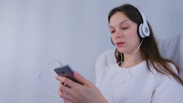 Mulher está ouvindo música em fones de ouvido no smartphone e cantando uma música . — Vídeo de Stock