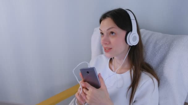 Mujer está escuchando música en los auriculares en el teléfono inteligente y cantando una canción . — Vídeos de Stock