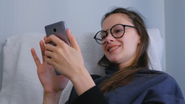 Lycklig kvinna är Bläddra och titta i sociala medier i smartphone i glasögon. — Stockvideo