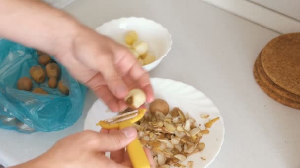 Манные руки очищают картофель с помощью желтой кожуры. Картофель выпадает из рук — стоковое видео