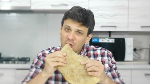 Jonge man in een plaid shirt eet een grote cheburek met een eetlust. — Stockvideo
