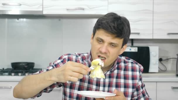 Jovem de camisa xadrez comendo ovos mexidos sentados à mesa . — Vídeo de Stock