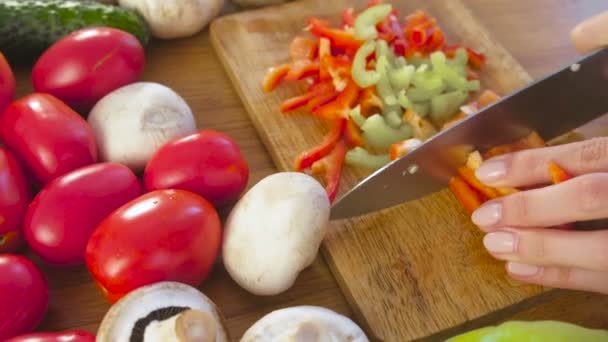 Le mani delle donne stanno tagliando il pepe rosso e verde su tavola di legno sul tavolo della cucina con verdure . — Video Stock