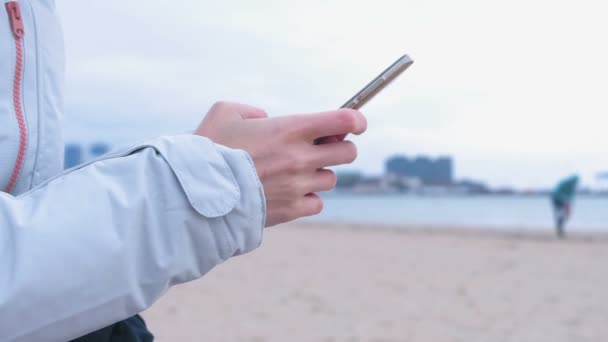 Frauen in Großaufnahme tippen am Telefon eine Nachricht auf Meeresgrund. Meer Winter, Frau in weißer Jacke. — Stockvideo