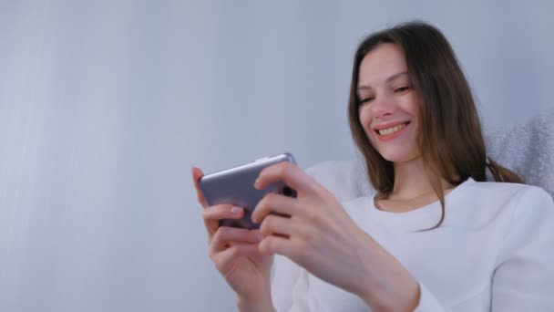 Mujer morena joven está jugando juego en el teléfono móvil . — Vídeo de stock