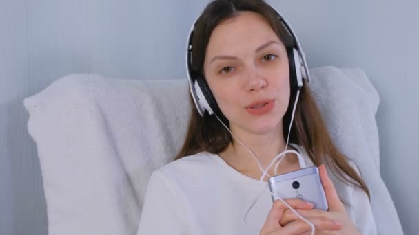 Frau hört Musik über Kopfhörer auf Smartphone und singt ein Lied. — Stockvideo